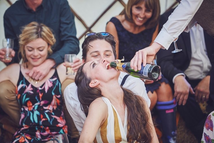 guest having fizz poured sown her throat at a boho wedding in Dorset